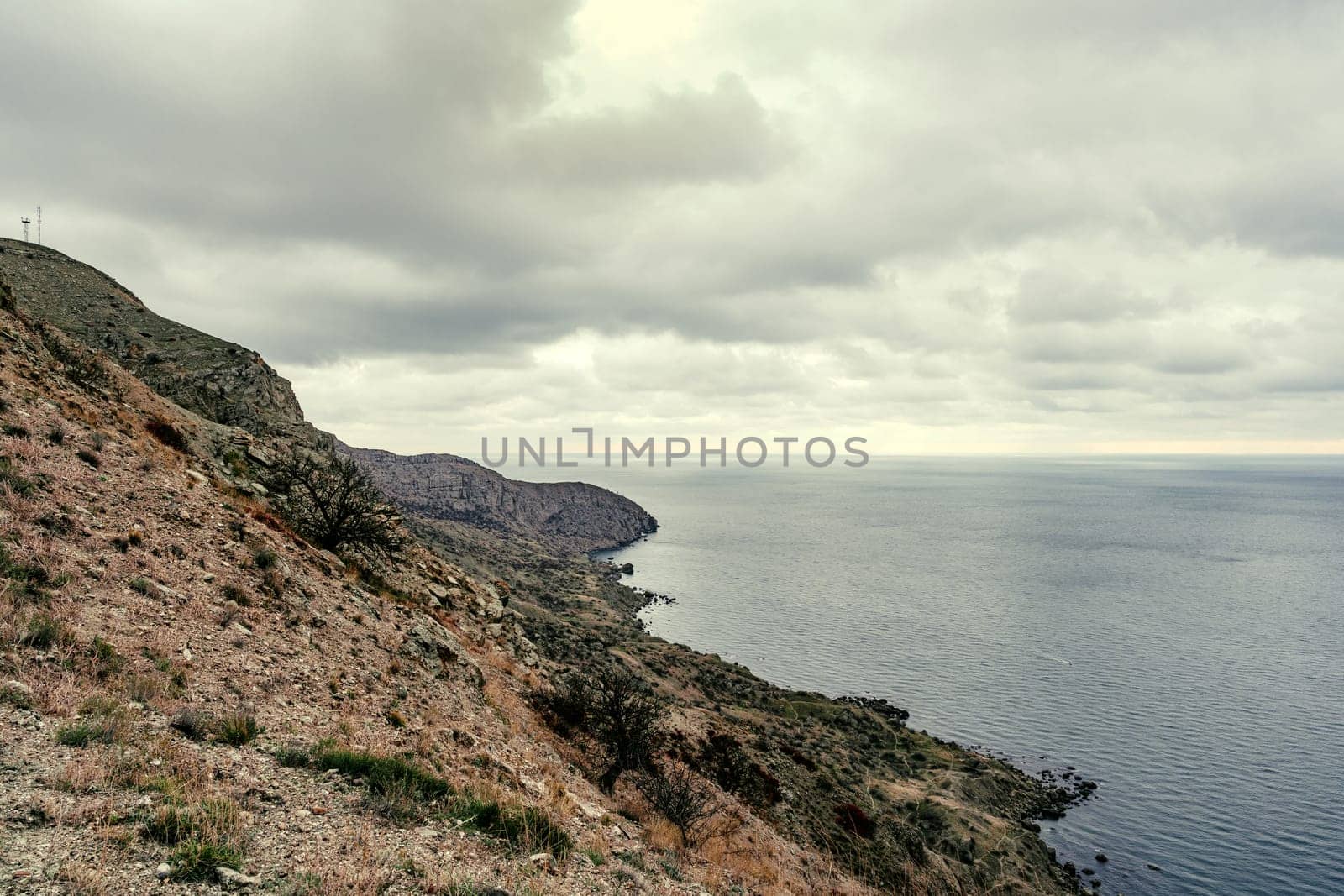 Lush cliffs descend into a calm sea on a cloudy day, showcasing the natural beauty of the coastal region. The landscape reveals a serene atmosphere and earthy tones.