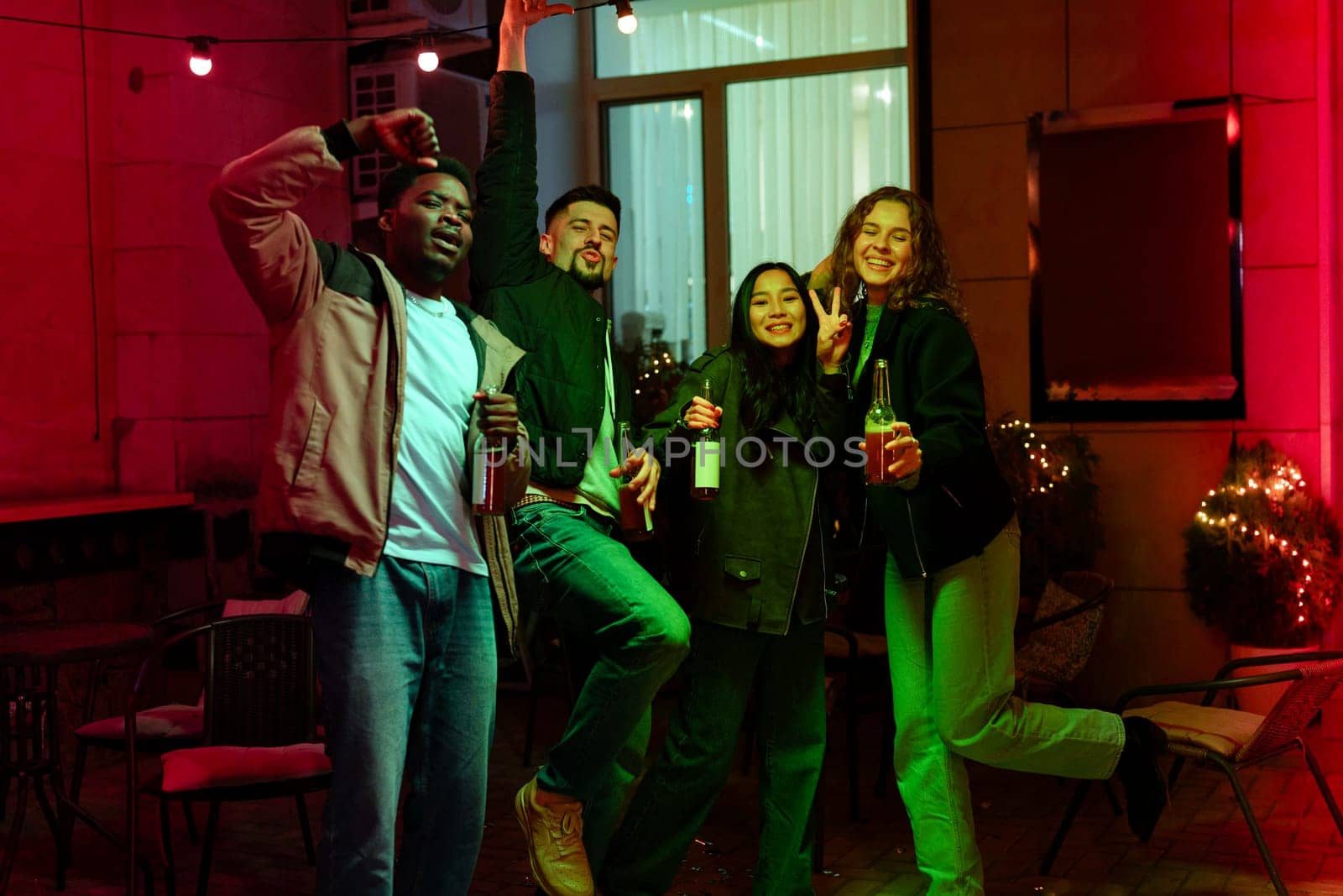 Groups of friends enjoy a lively evening gathering filled with laughter and drinks in a cozy outdoor space adorned with fairy lights, creating a festive atmosphere.