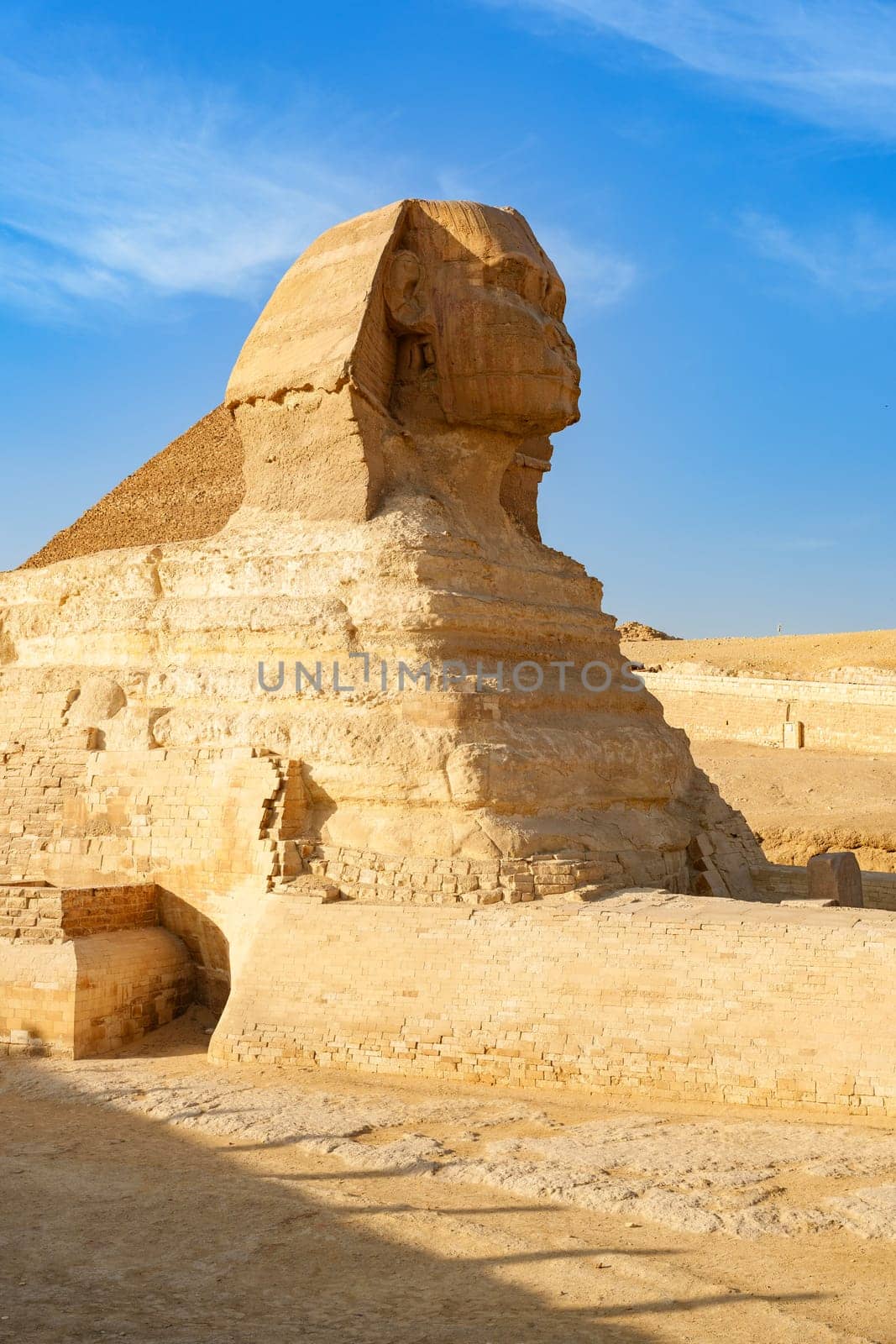The Great Sphinx stands majestically at Giza, showcasing its massive stone body and detailed features. The bright midday sun highlights the ancient monument's grandeur against a clear sky.