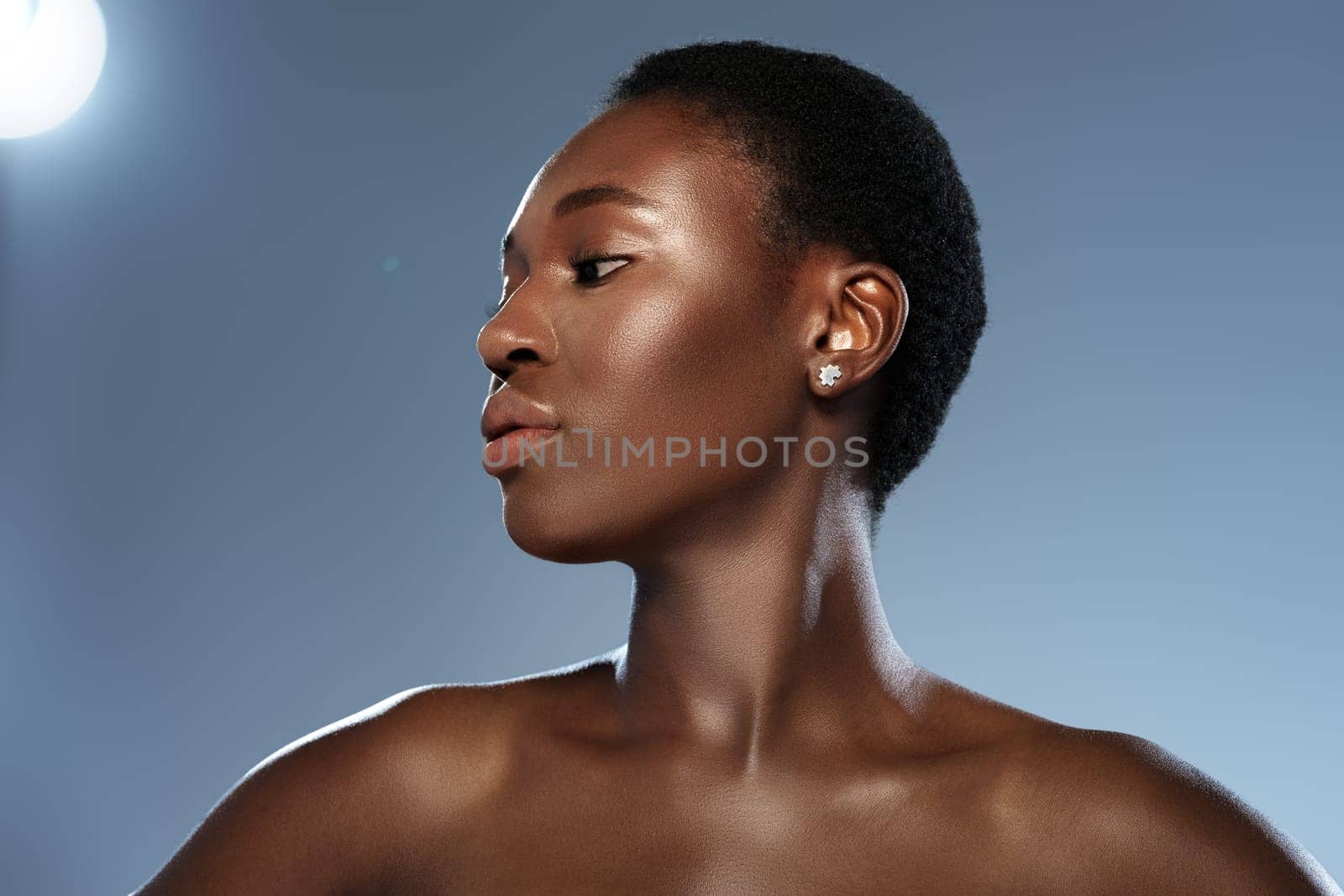 A woman with short, textured hair poses gracefully with her profile highlighted against a softly lit blue background. Her confident expression and subtle jewelry add elegance to the moment.