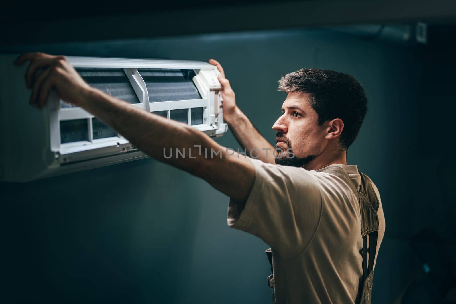 A technician carefully positions an air conditioning unit against the wall in a dimly lit room.