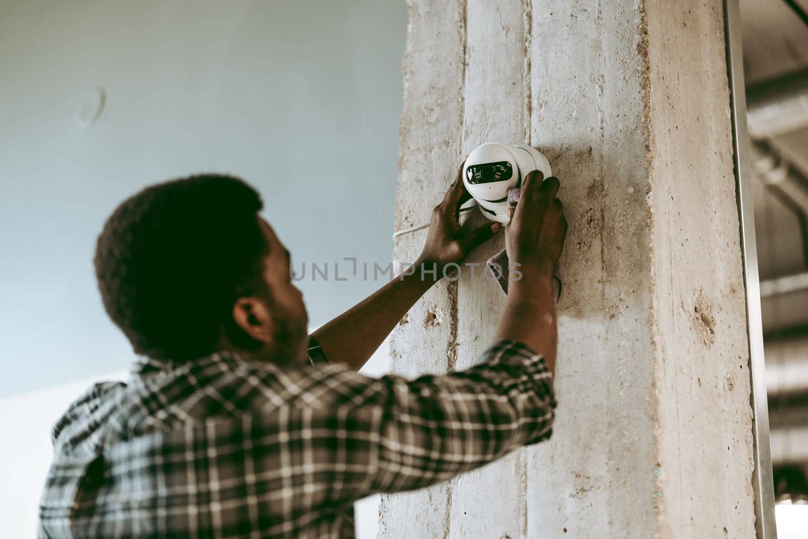 A technician focuses on installing a white security camera on a concrete pillar inside a bright, modern office. Tools and equipment are nearby as he works diligently.