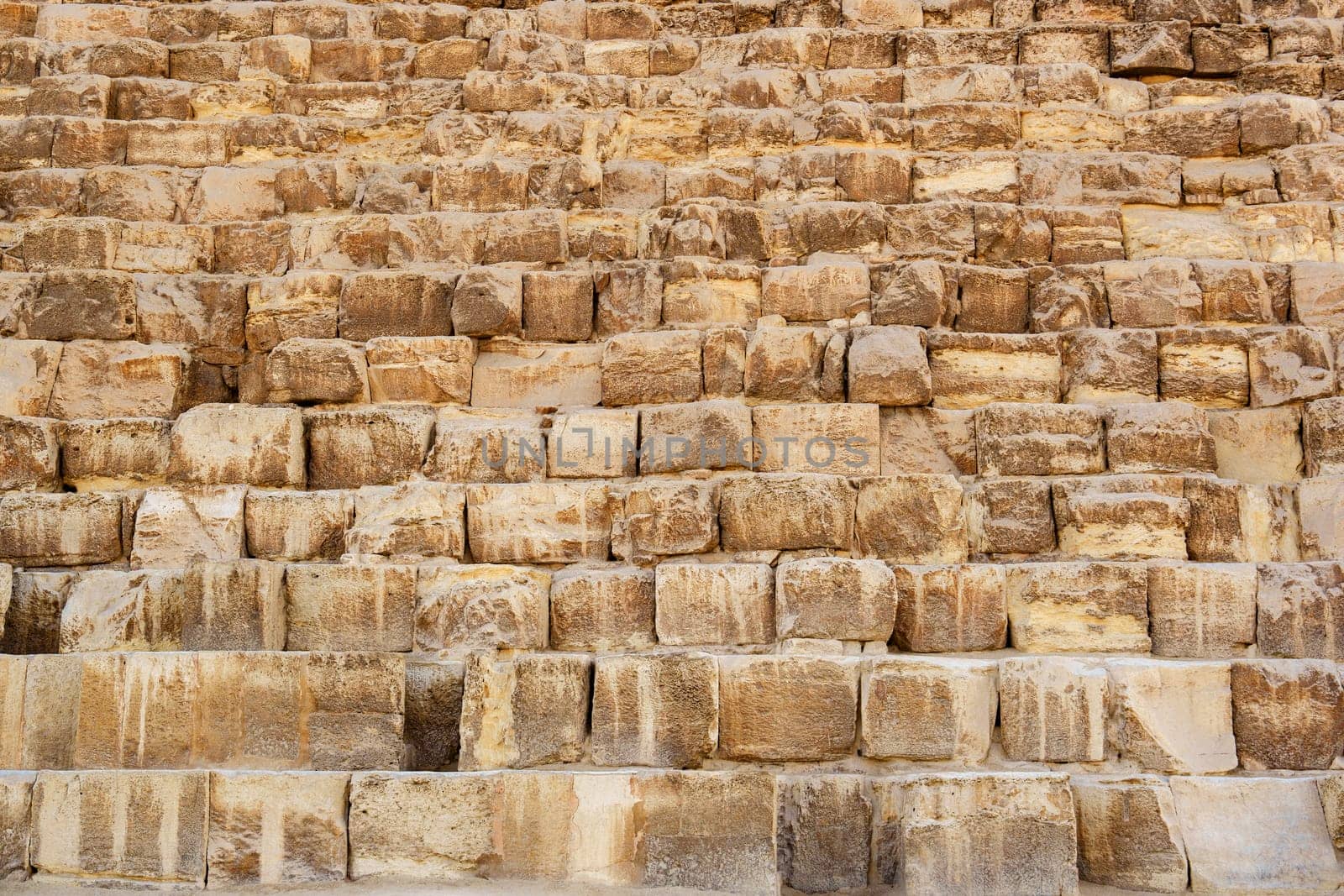 Visitors admire the ancient stone steps of the Great Pyramid, marveling at the intricate construction and historical significance of this monumental site in Egypt under a bright sun.
