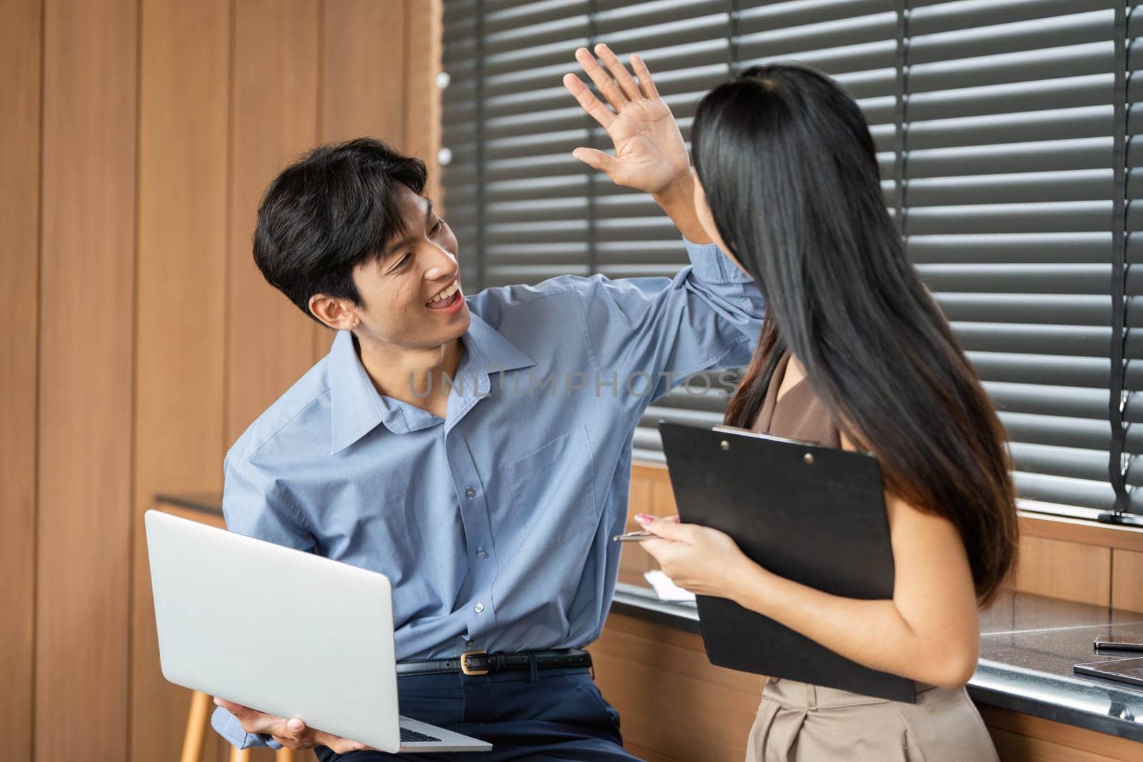 Two young professionals celebrate a successful collaboration with a high-five, showcasing teamwork and positive relationships.