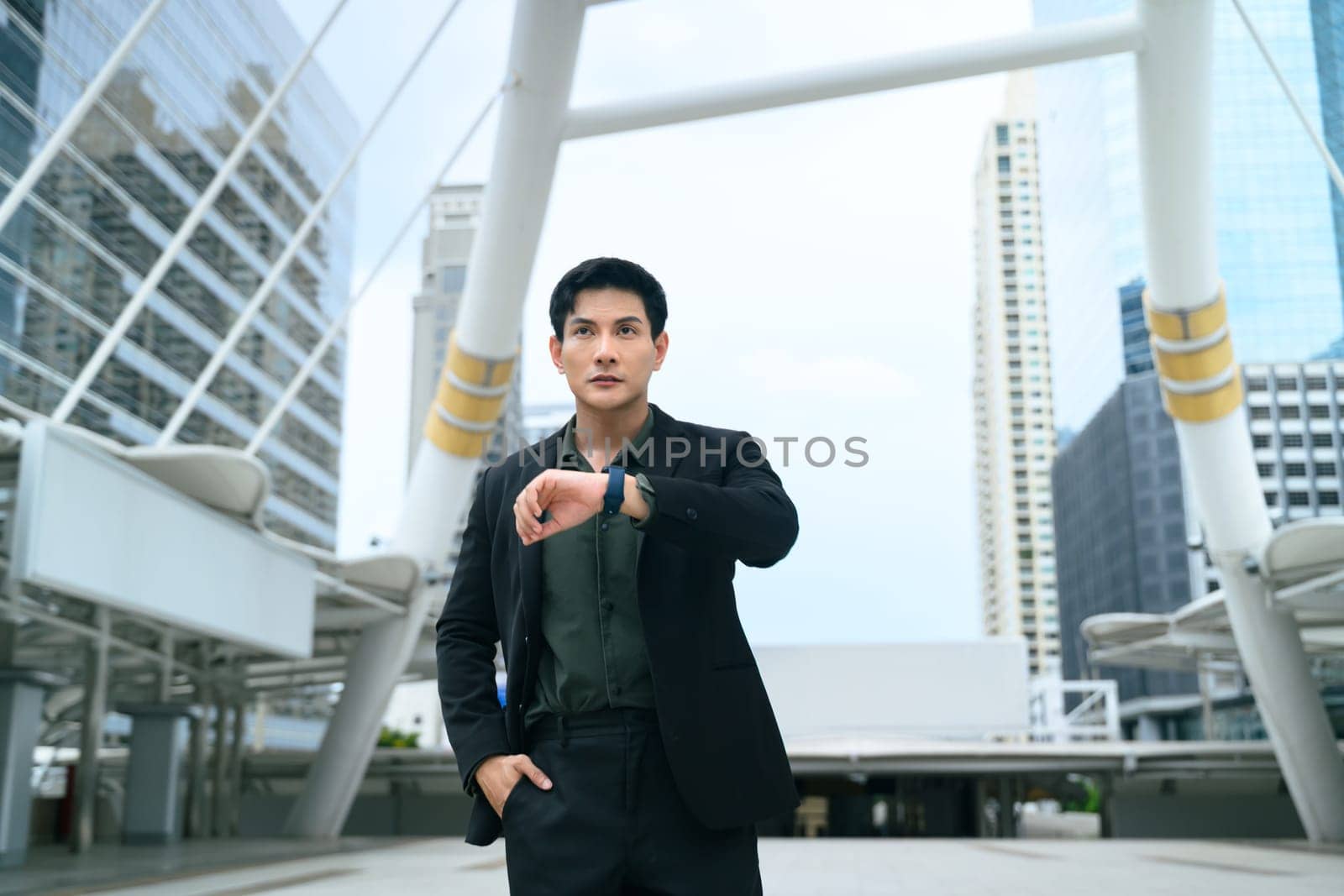 Confident businessman in a black suit looking at his smartwatch while standing in a modern urban.