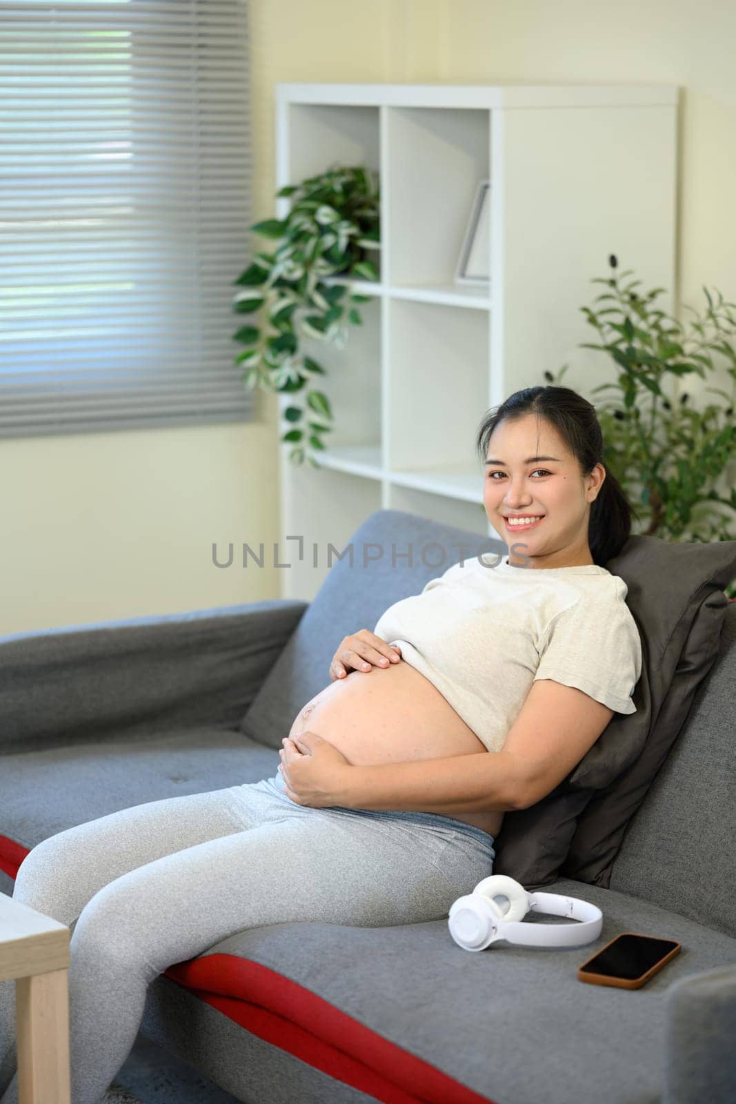 Smiling expectant mother resting on the sofa and gently holding her belly.