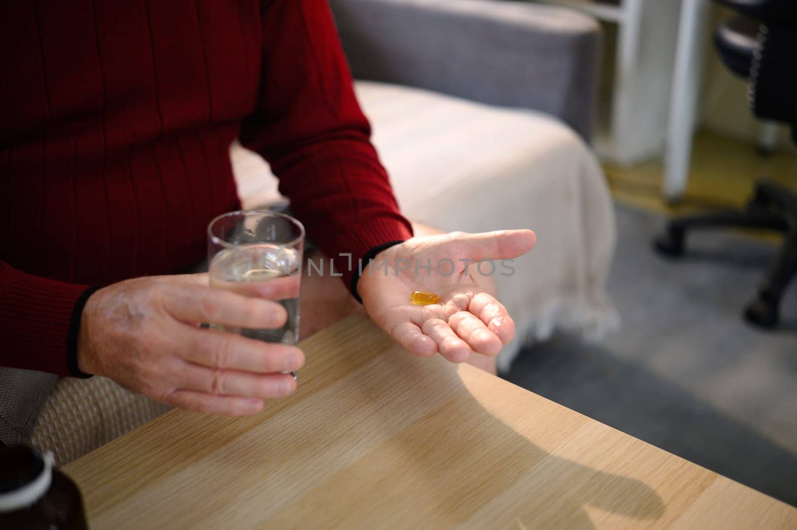 Close up of an elderly man holding a glass of water and pill.