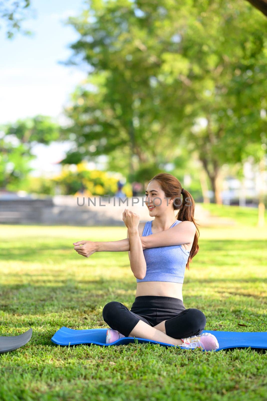 Smiling woman in workout clothes warms up for exercise on a grassy field.