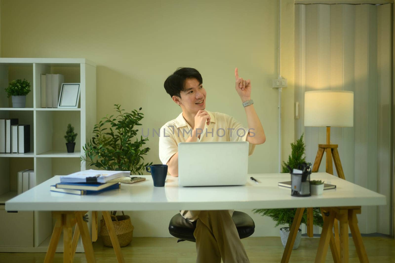 Smiling man entrepreneur sitting at working desk and pointing finger up.