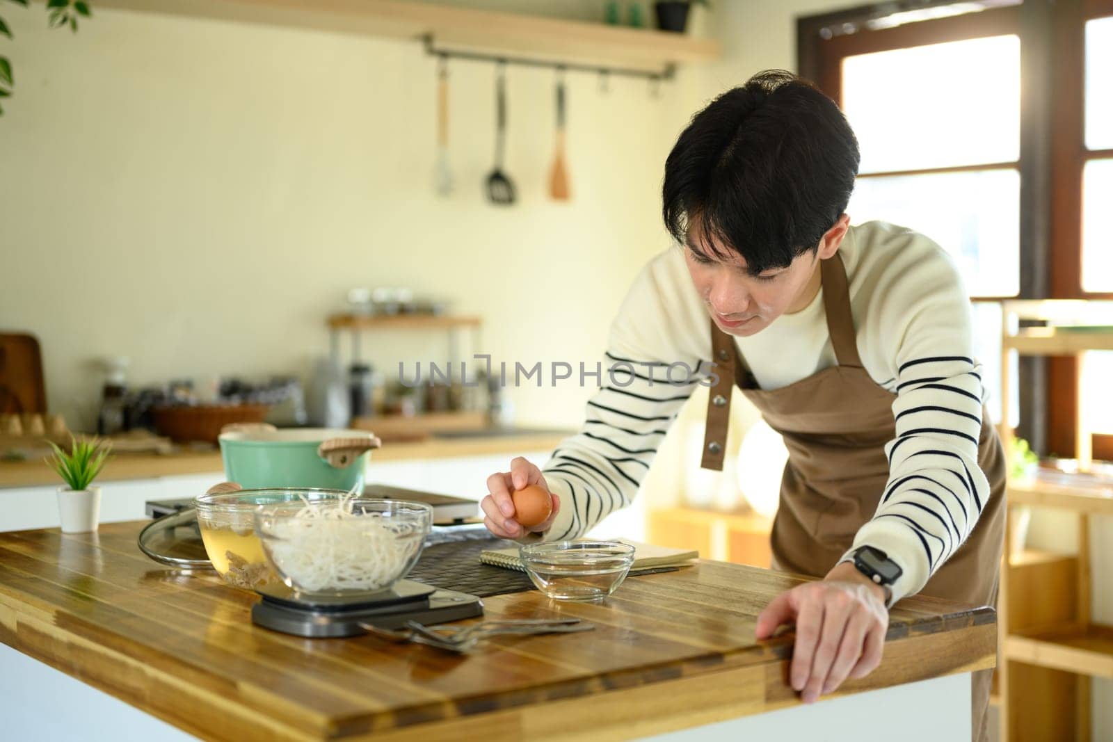 Happy Asian man cooking at home with fresh ingredients.