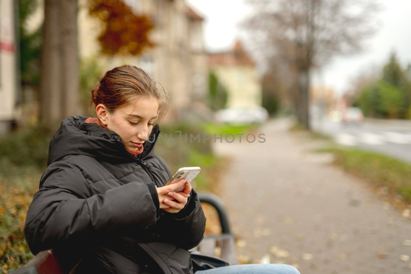 Sweet Girl Scrolling Phone While Sitting On Bench Outside