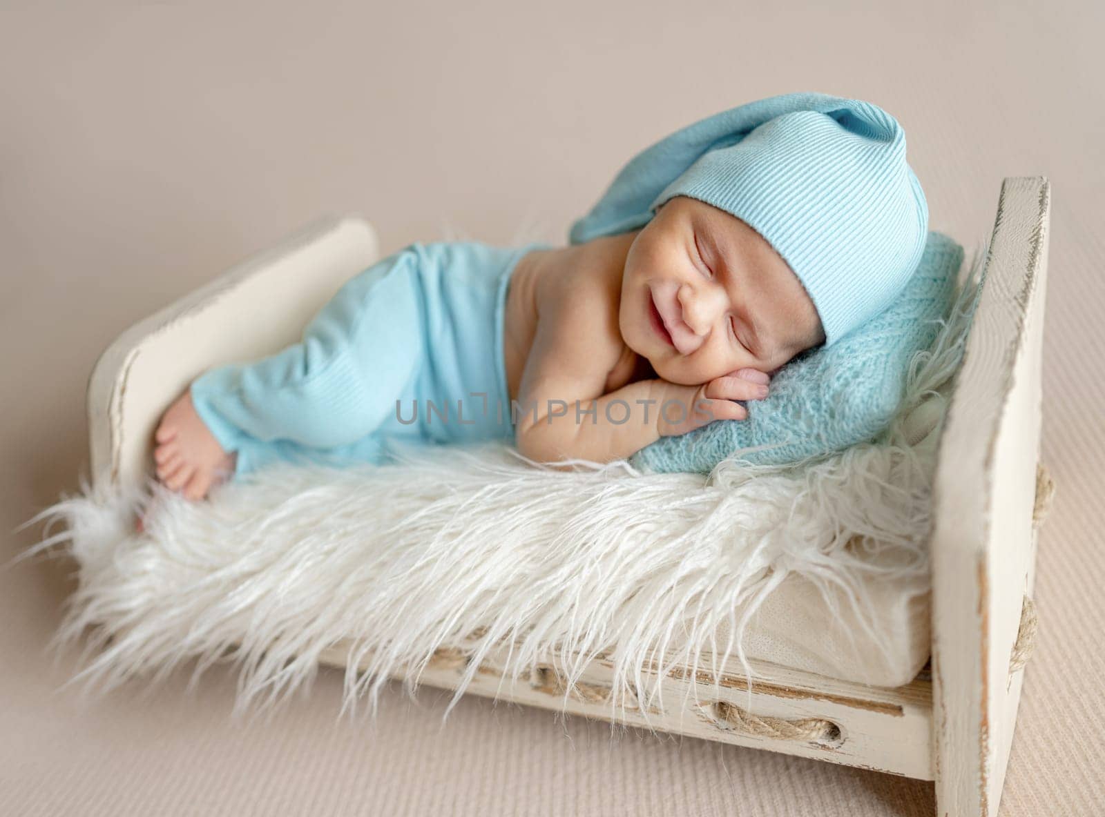Newborn Baby Sleeping With Adorable Smile On A Little Bed In The Photo Studio