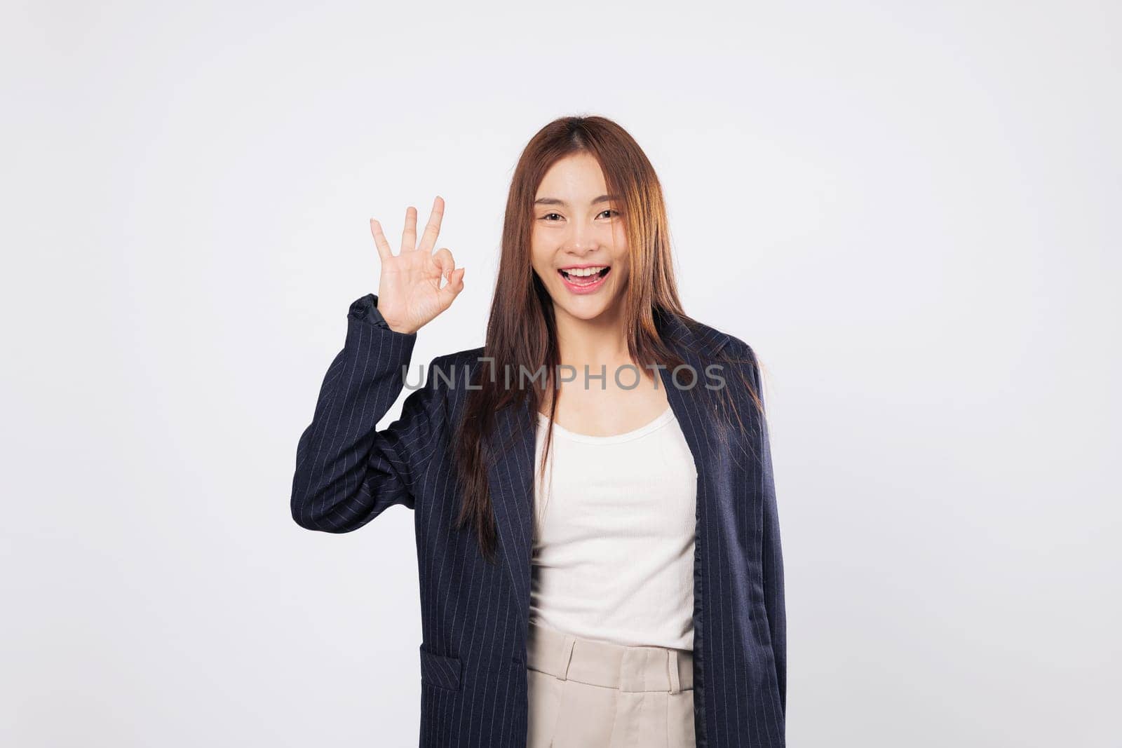 OK sign ok approval by a happy Asian woman smiling and gesturing success with her fingers isolated on a clean white background showing confidence and business agreement