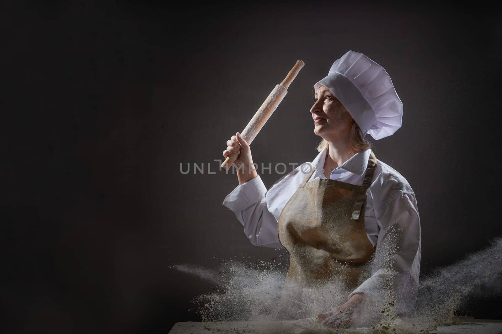 An elderly cook playfully poses with a rolling pin, surrounded by flour, capturing a lighthearted moment in her kitchen.