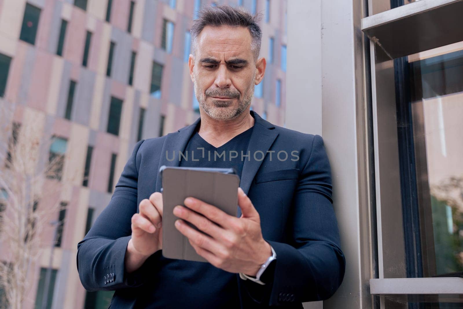 Confident businessman standing outdoors using a tablet in a modern urban setting. He appears focused and professional. Concept of digital work, technology, and contemporary business lifestyle.