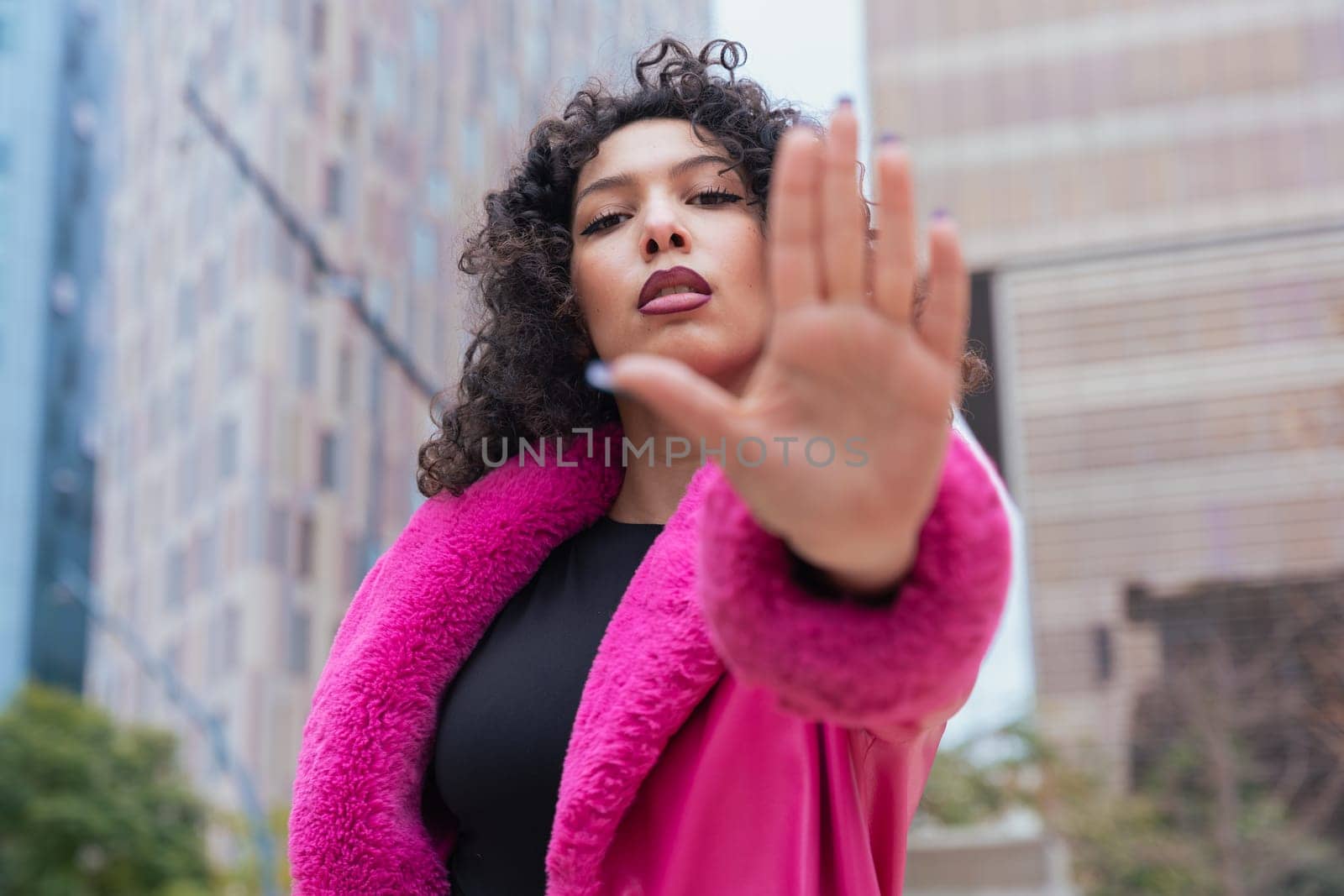Graceful dancer with curly hair wearing a pink coat, expressing movement and energy in an urban environment. Modern fashion, contemporary dance, and artistic performance against a city backdrop.