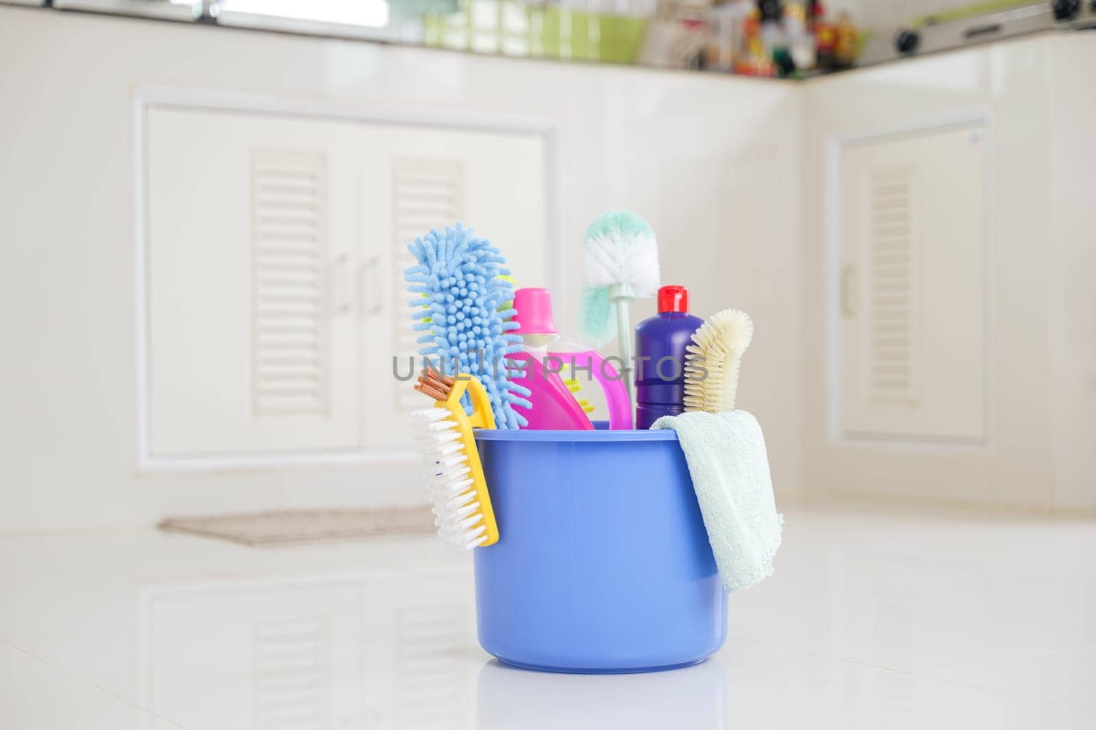 House cleaning essentials. A plastic bucket with detergent, brushes, and supplies sits on the kitchen floor, making routine cleaning tasks easier and more efficient.