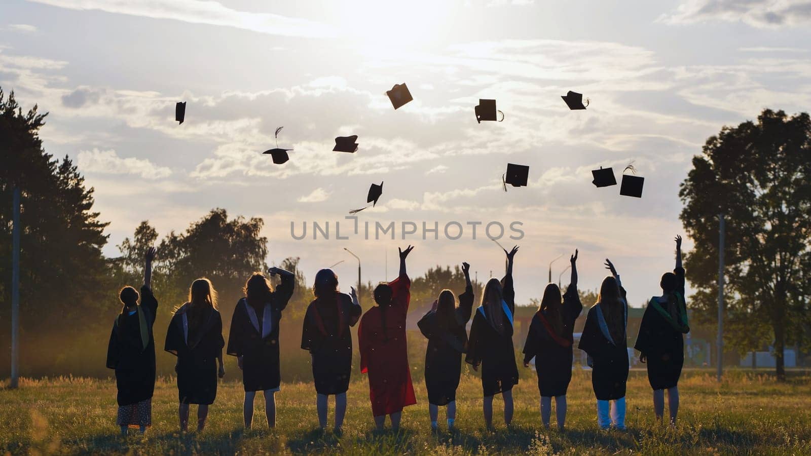 Group of students joyfully celebrating graduation, tossing their caps high into the air against a stunning sunset backdrop