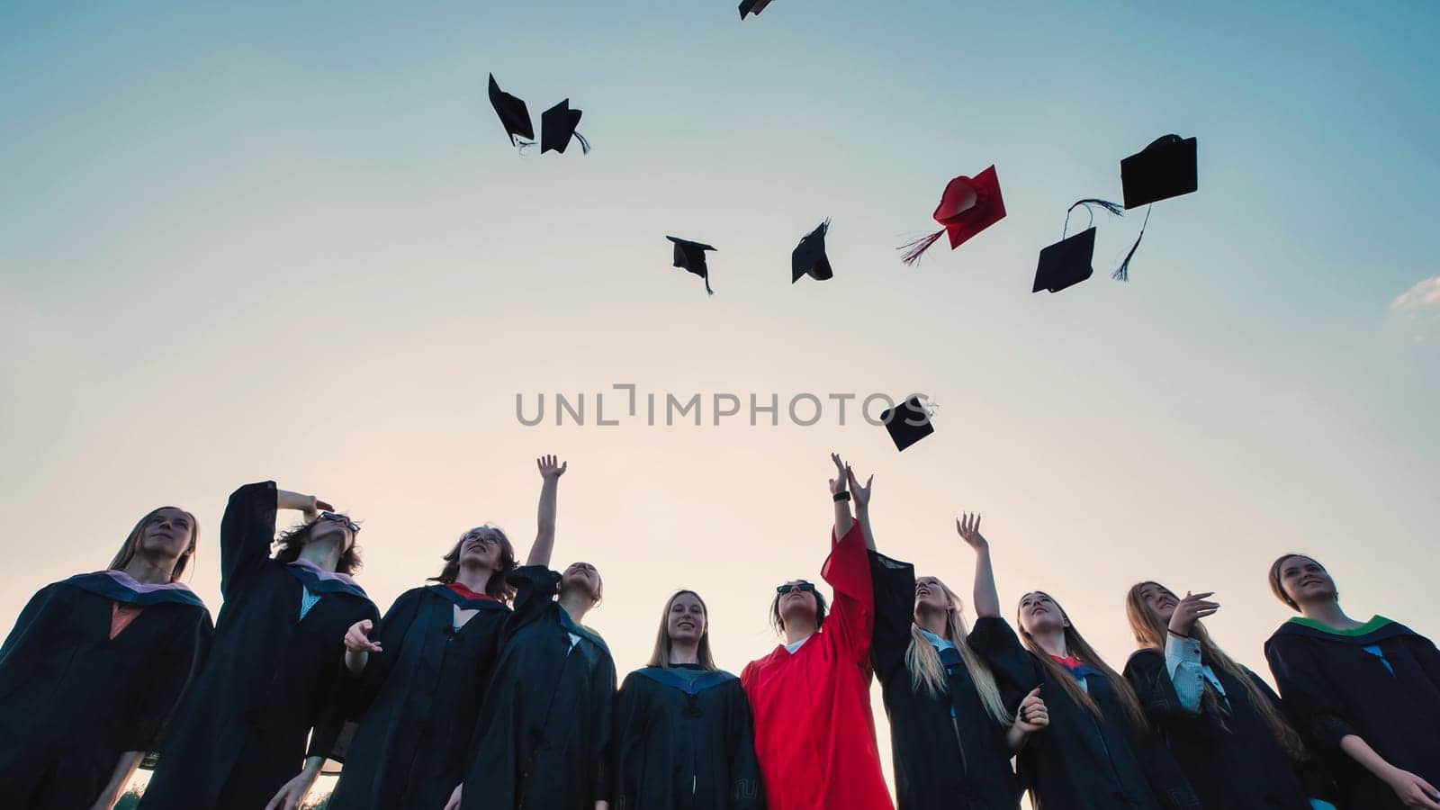 Group of cheerful graduates celebrating their graduation by tossing their caps into the air against a beautiful sunset sky