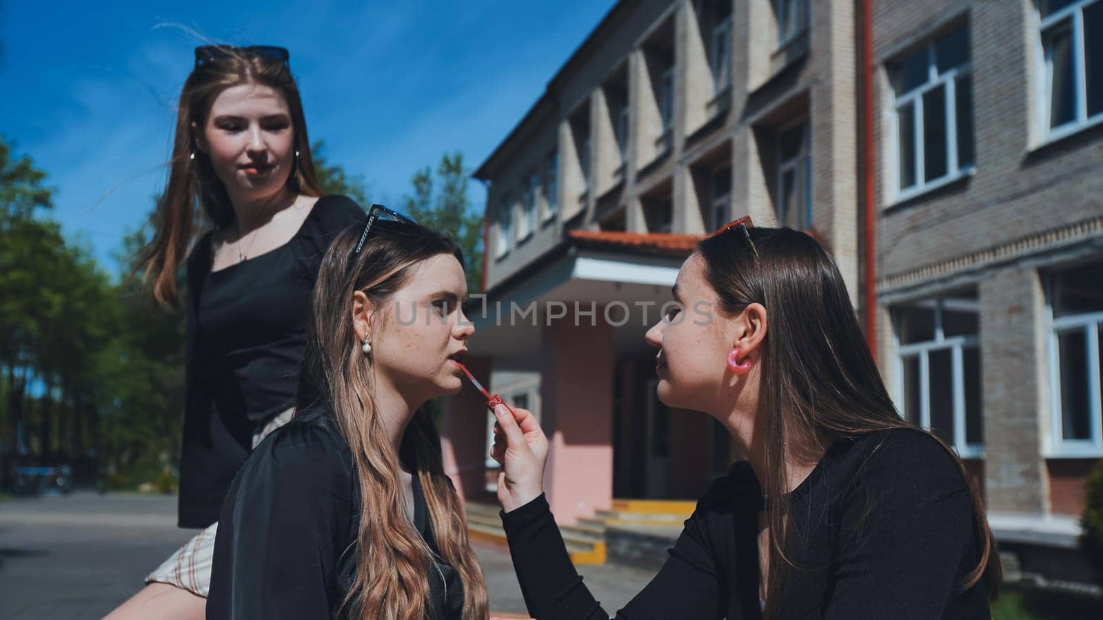 High school students putting on lipstick in the schoolyard during their break, getting ready for the next class