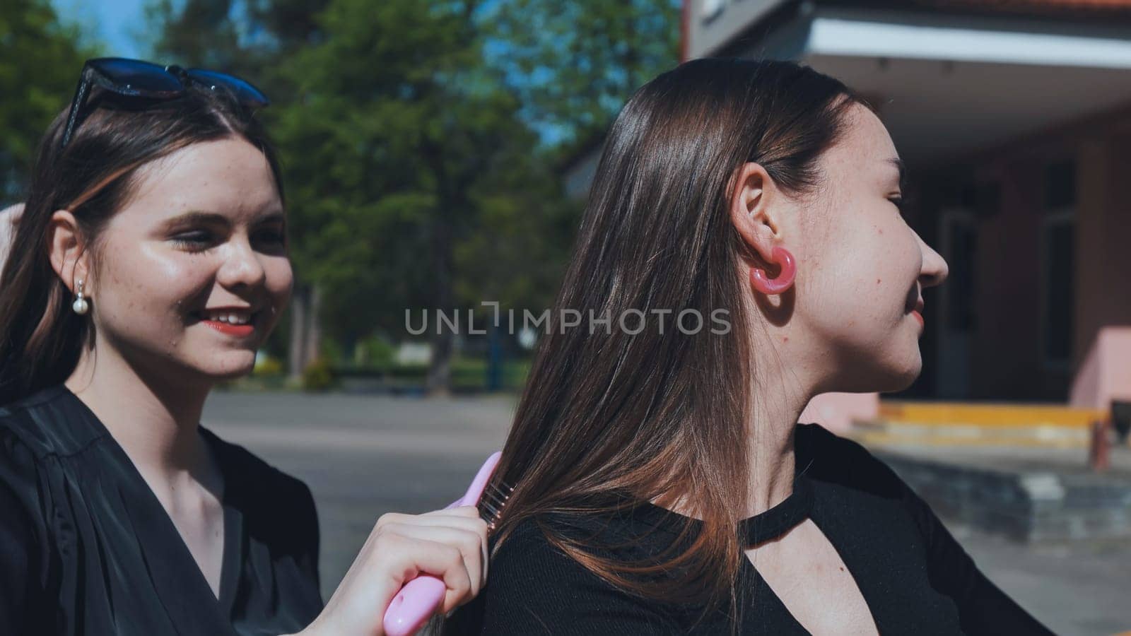 Two teenage friends bonding after school, one gently brushing the other's hair with a pink brush on a sunny afternoon
