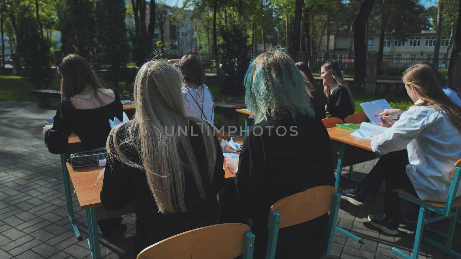 Group of high school students sitting at desks outdoors, learning and studying together on a bright sunny day