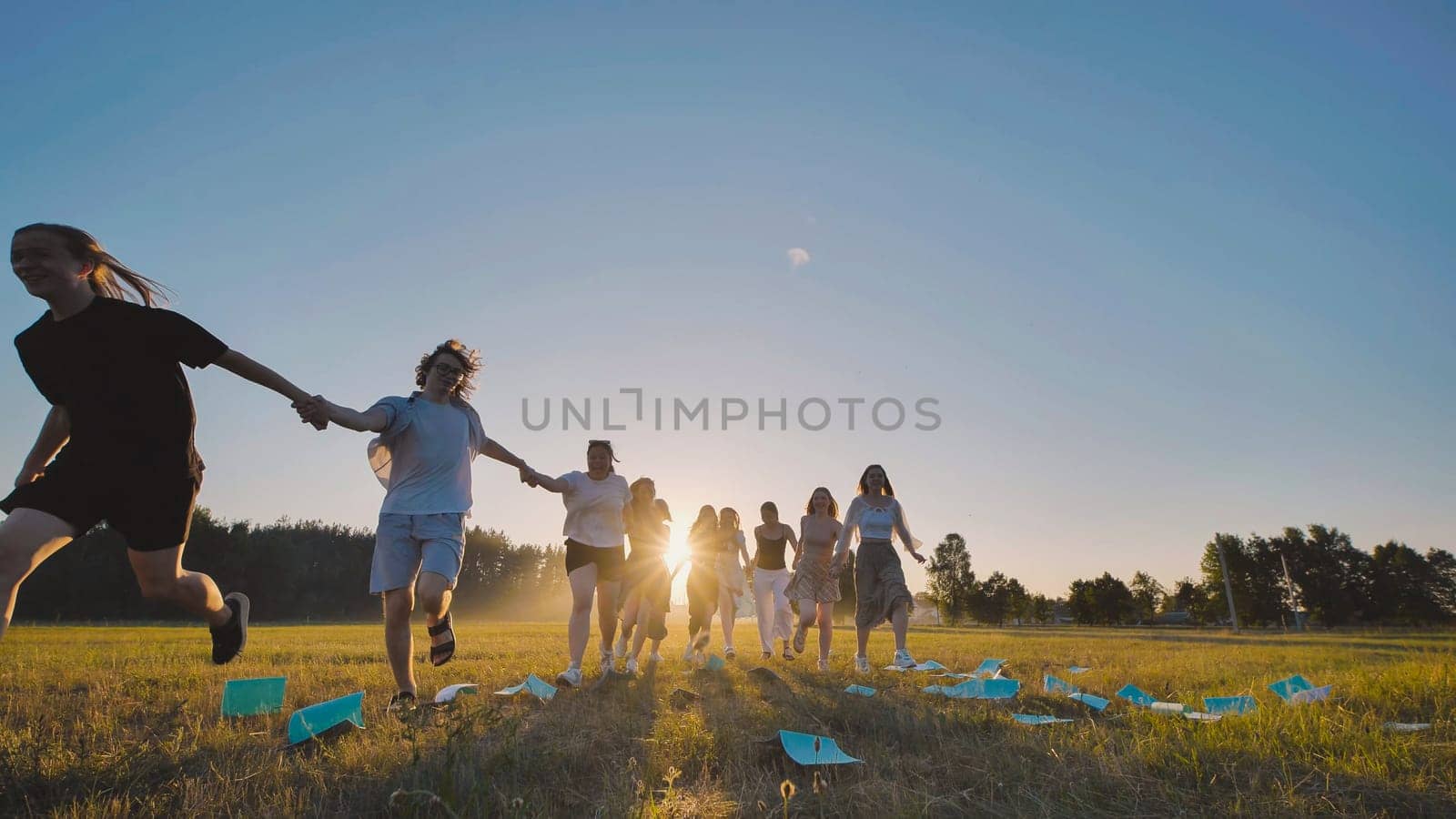 Teenagers joyfully sprinting towards the setting sun in a meadow, gleefully tossing papers into the air to mark the end of the school year