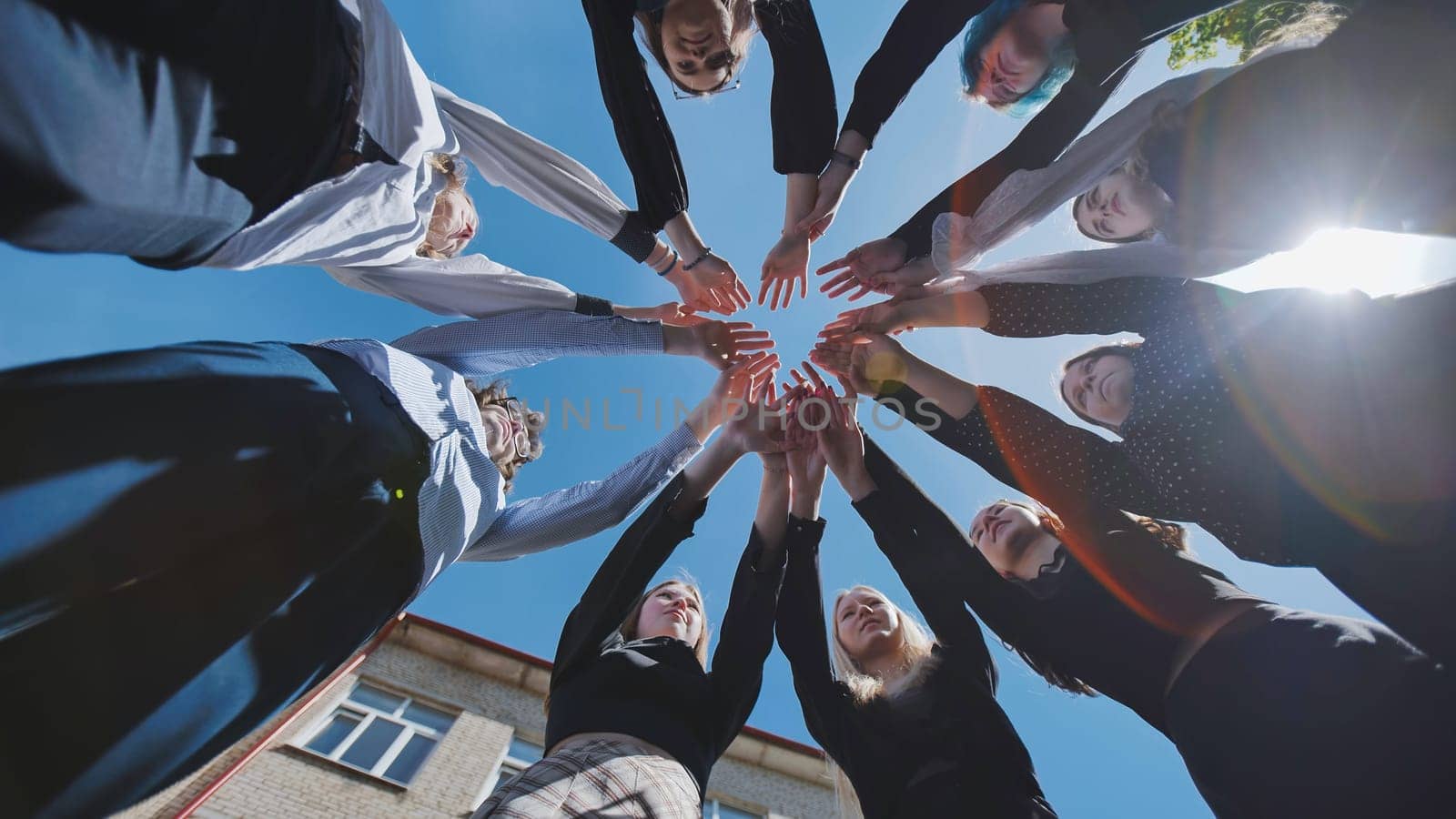 Group of students forming a circle joining their hands together in the schoolyard, celebrating their school day