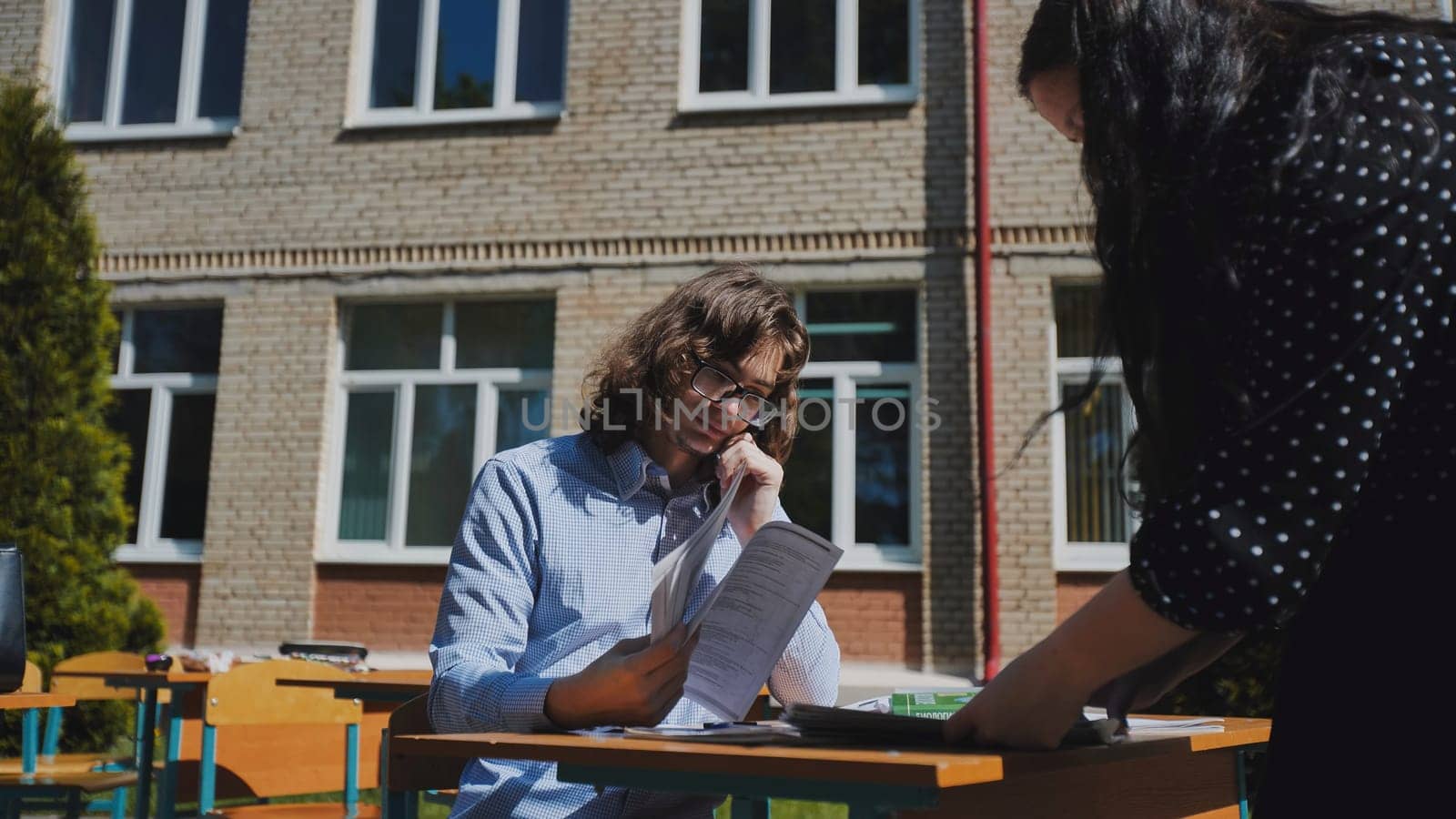 Two students are seen studying together at a schoolyard desk, getting ready for exams on a bright and sunny day