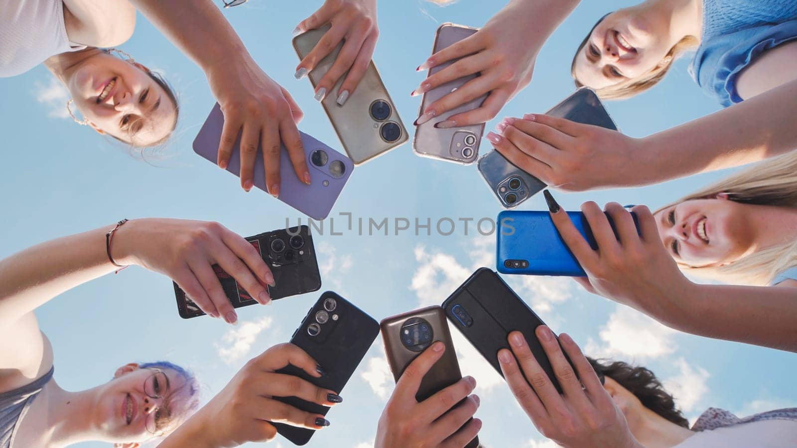 Group of happy students holding smartphones, making a circle with their devices, and enjoying their time together