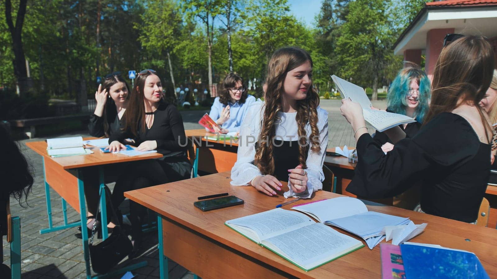 High school or university students are studying together at desks outdoors, sharing notes and enjoying the fresh air