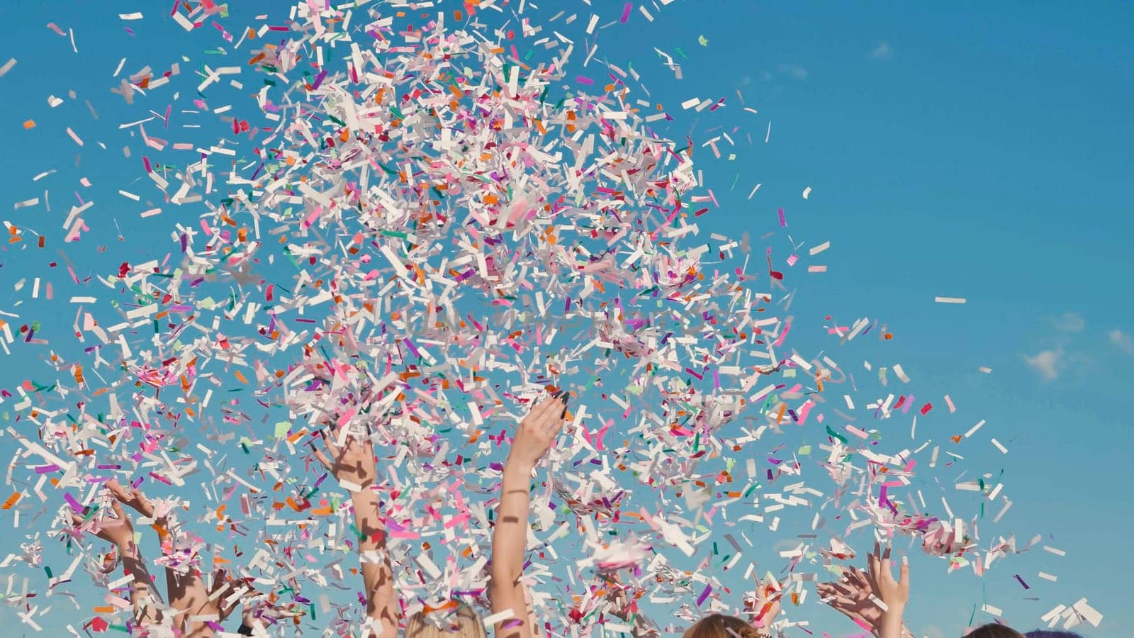 Group of cheerful high school students throwing colorful confetti in the air celebrating graduation under a bright blue sky