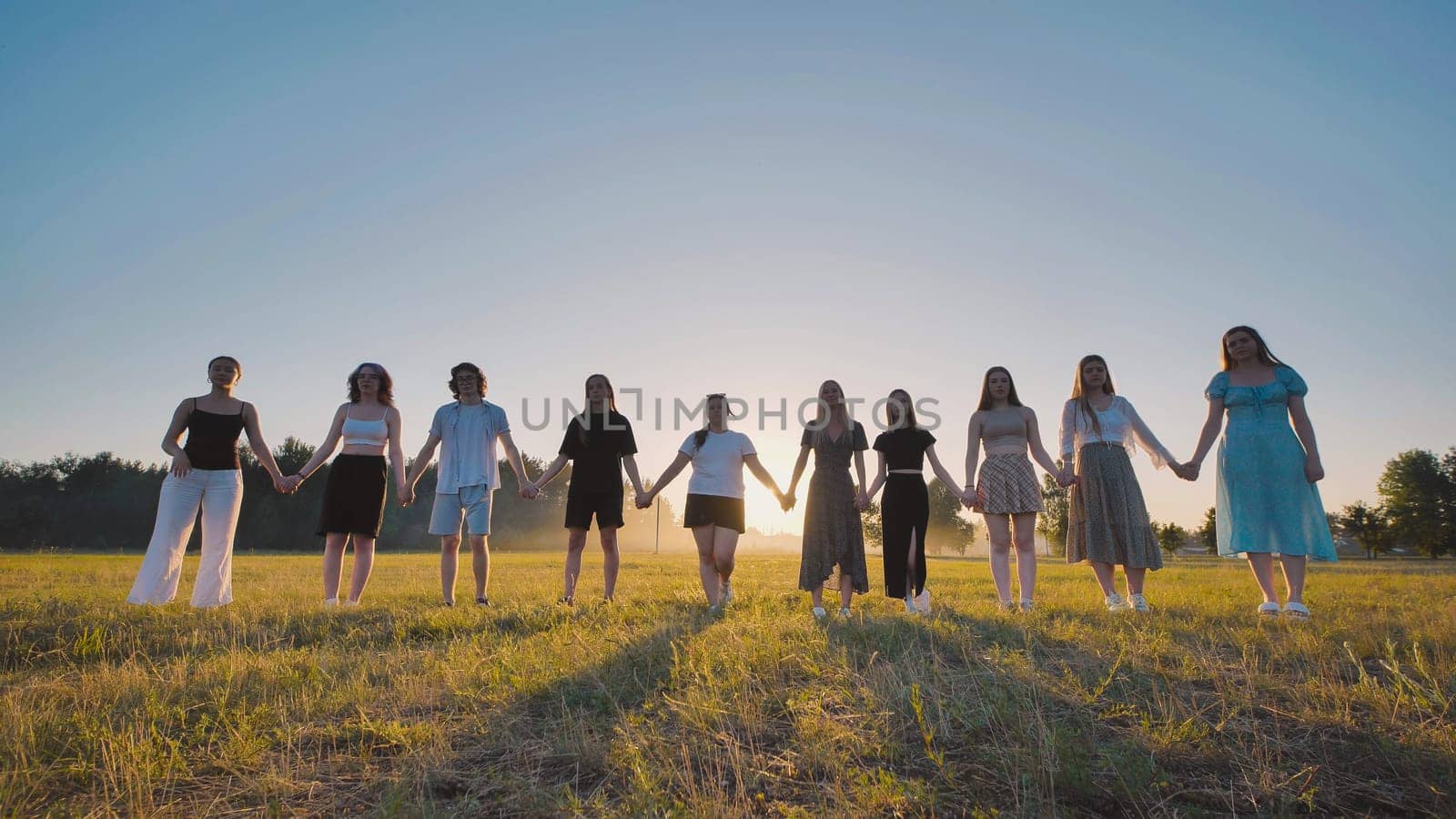 Group of friends are holding hands while standing in a field at sunset, celebrating their graduation