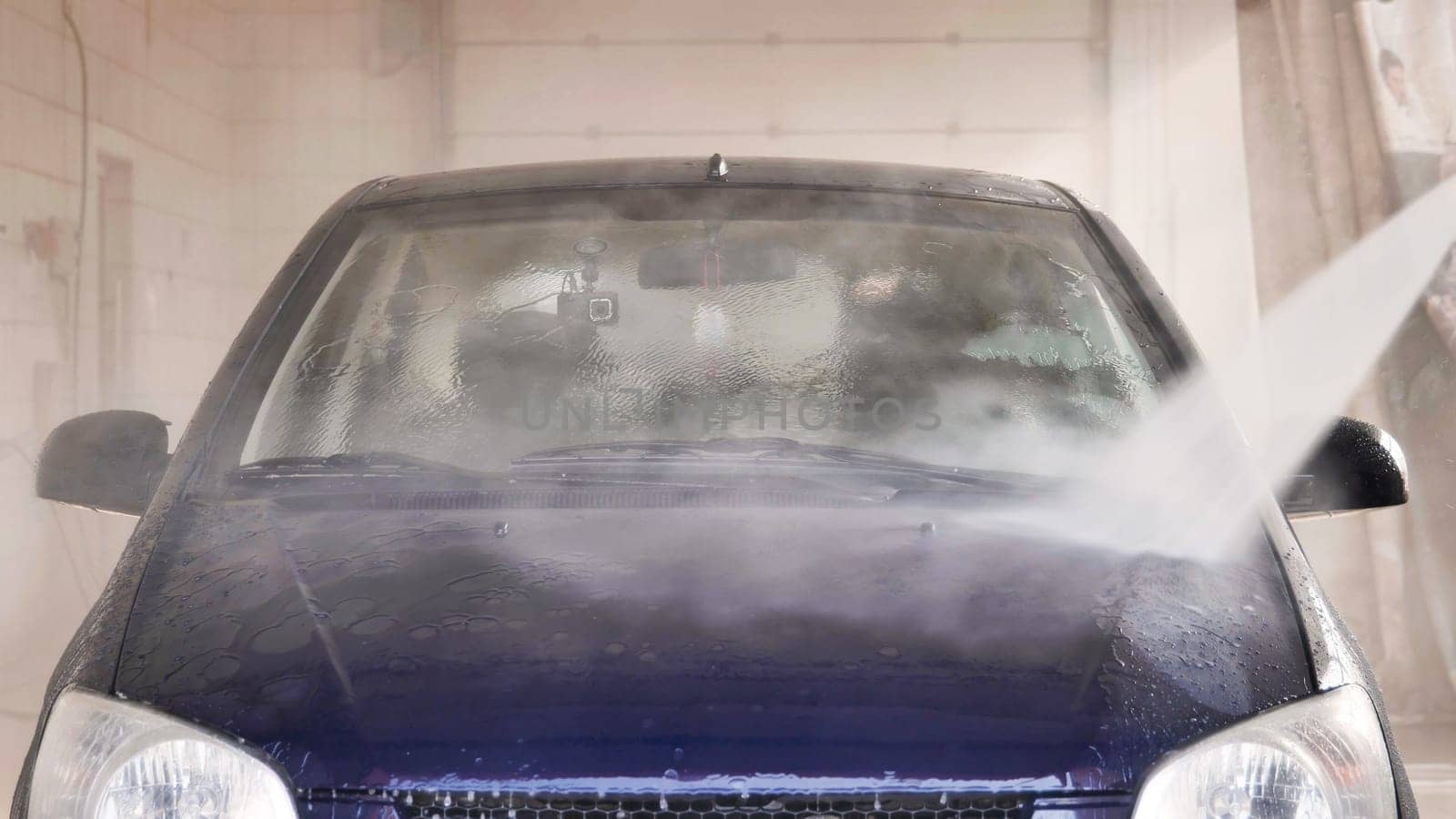 Car wash worker cleaning windshield with high pressure water jet during a car wash