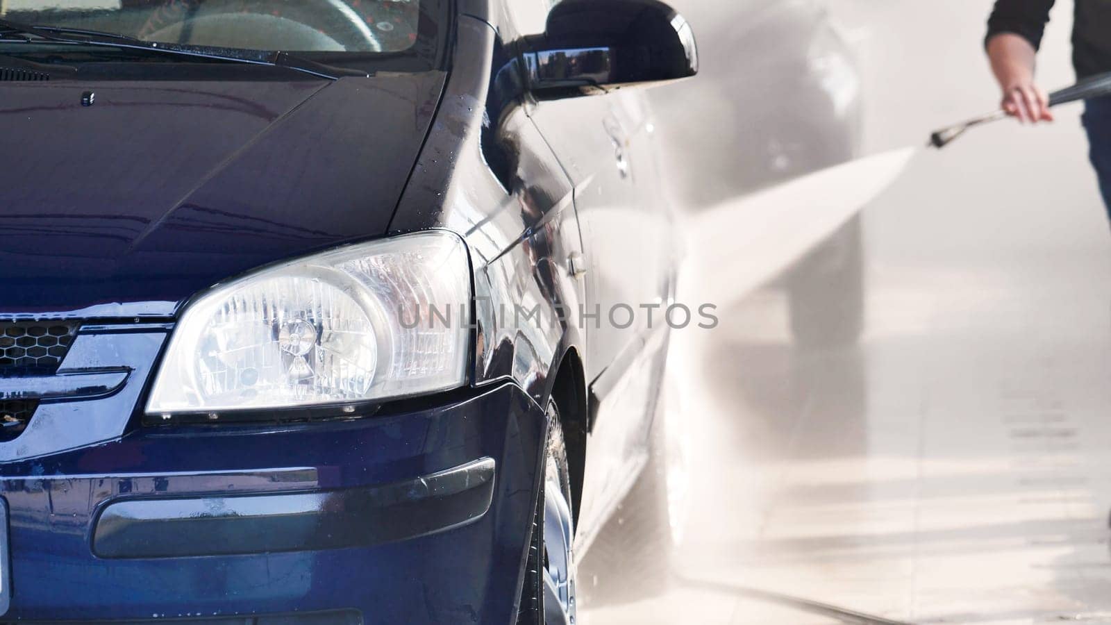 Car wash worker is using a high pressure water jet to clean a vehicle