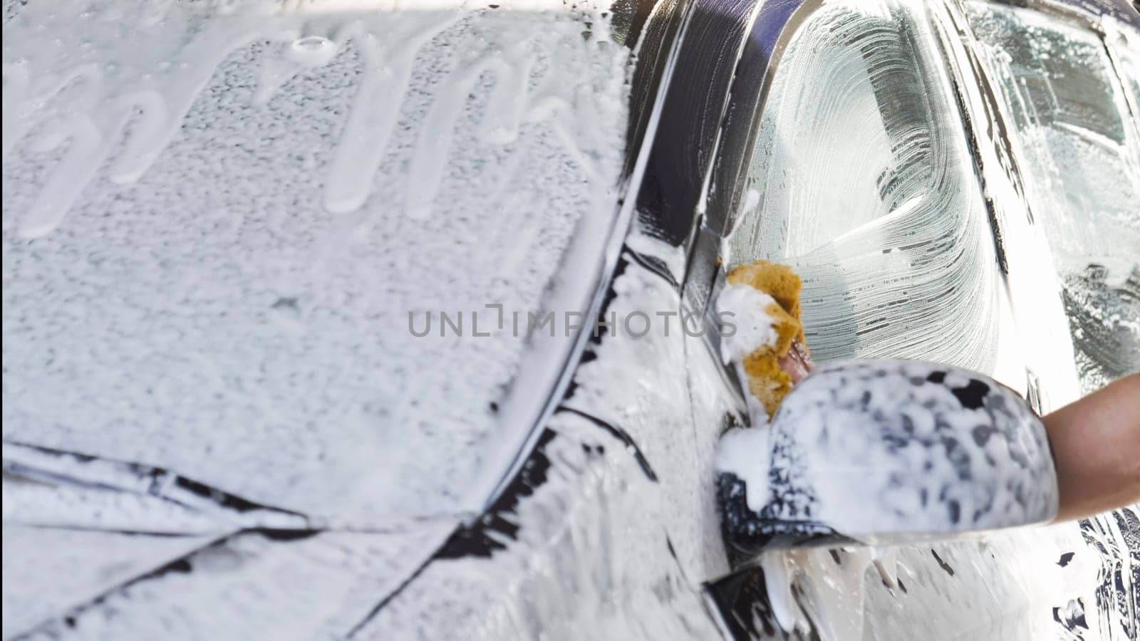 Car wash worker is cleaning a vehicle with a sponge and soap