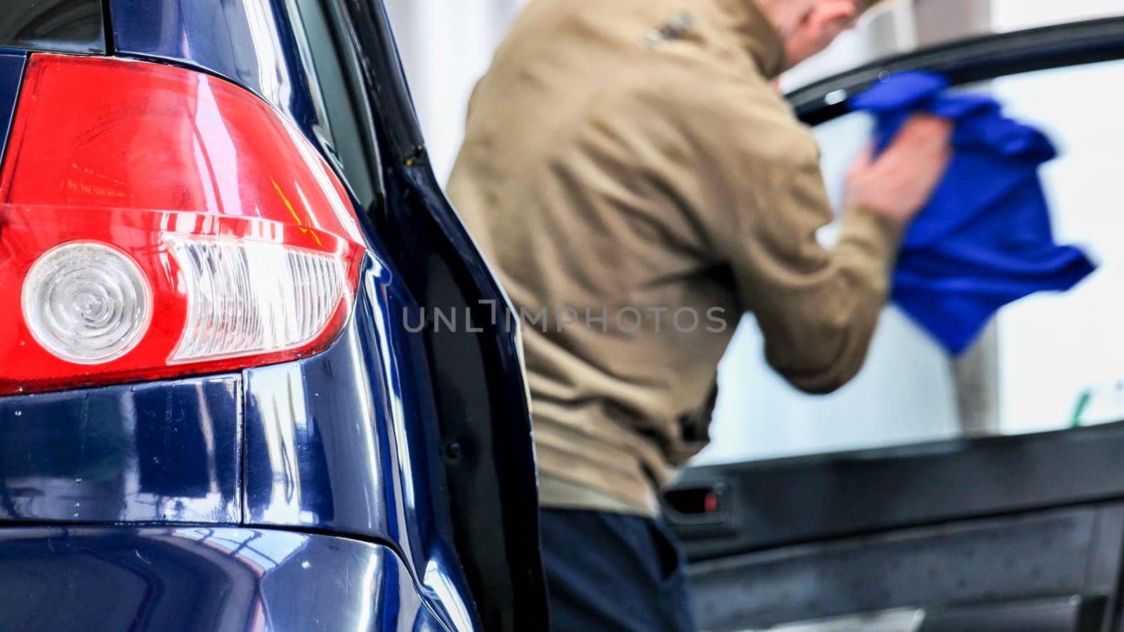Professional car wash service, employee cleaning vehicle window with microfiber cloth