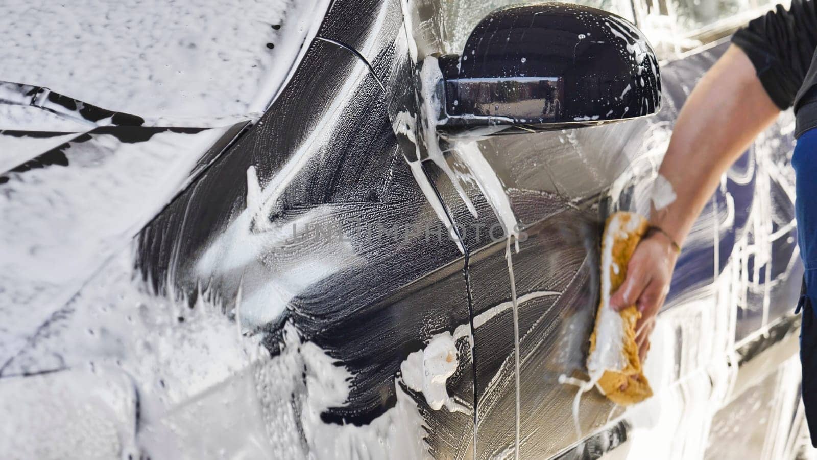 Car wash worker is cleaning a vehicle with a sponge and soap