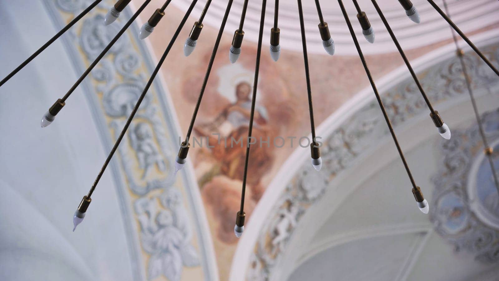 Low angle view of a modern chandelier with small light bulbs hanging in a church, illuminating a fresco on the ceiling