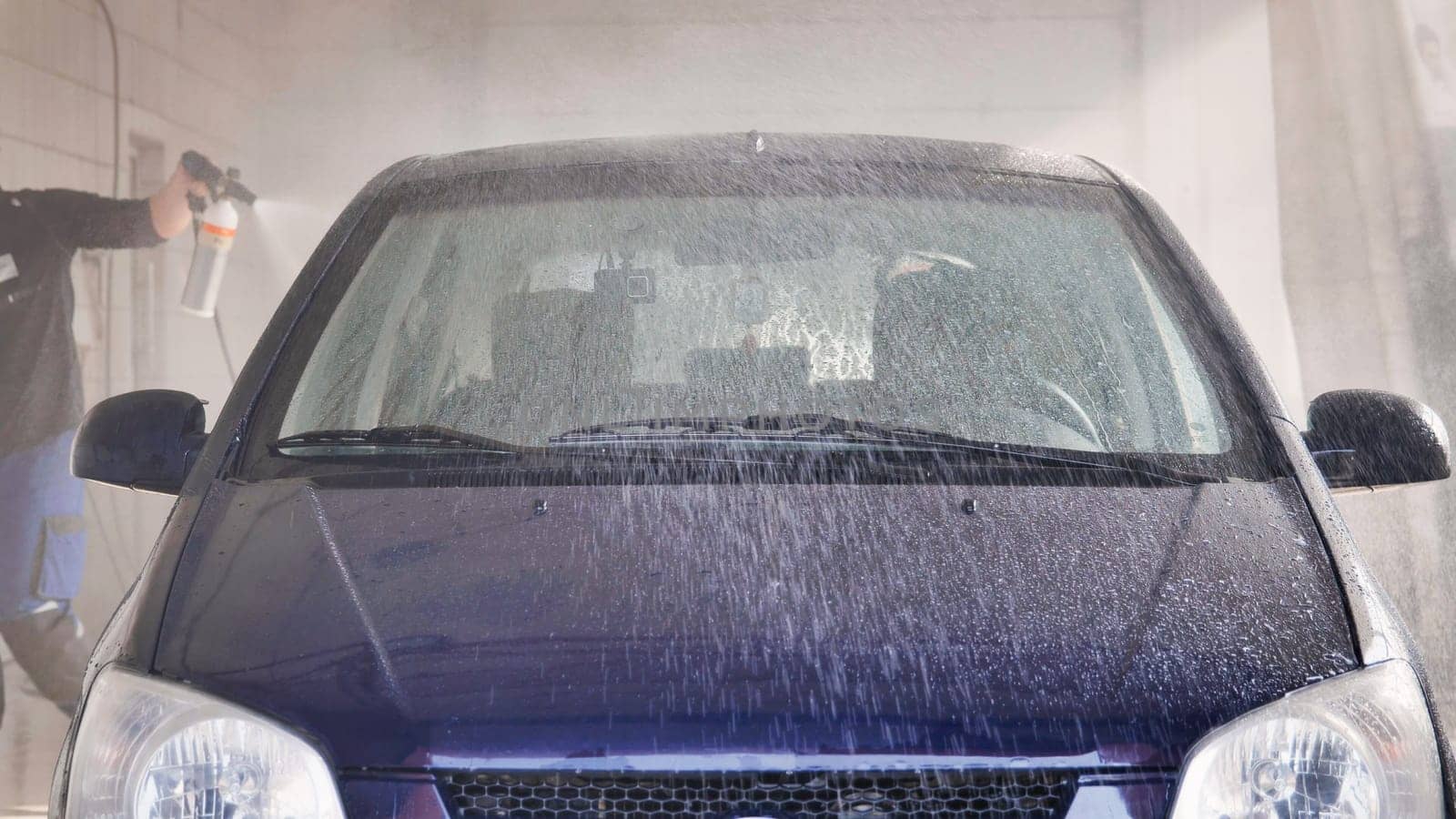 Car wash worker spraying pressurized water on a car during cleaning