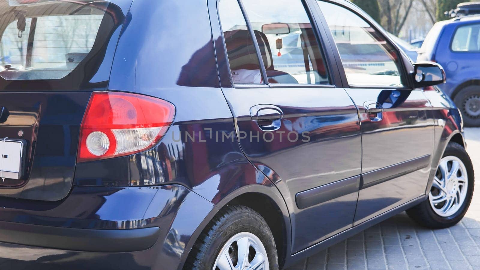 Freshly washed dark blue car gleaming under sunlight, parked on paved city street