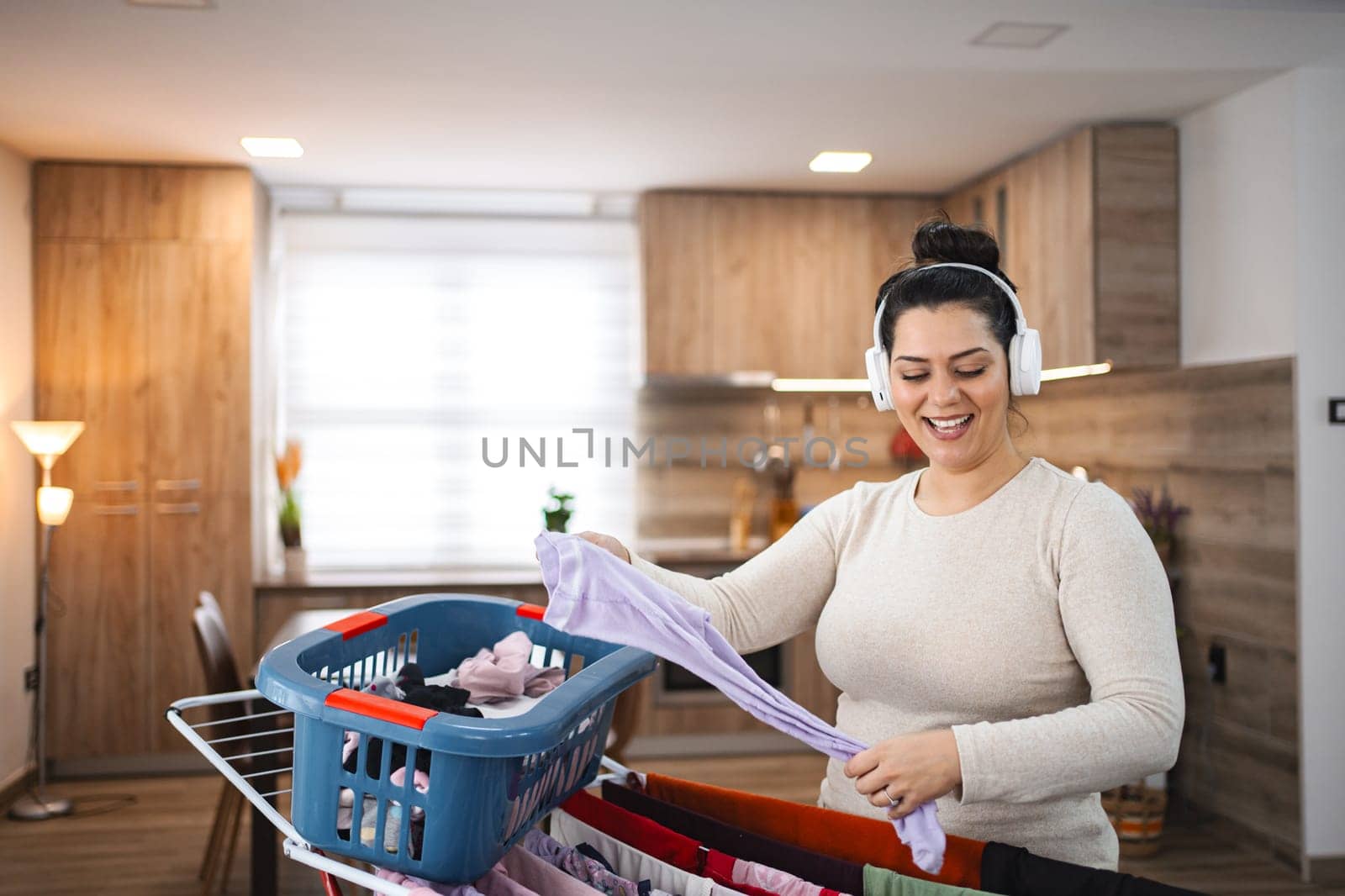 Woman listening to music while hanging the laundry on drying rack at home.