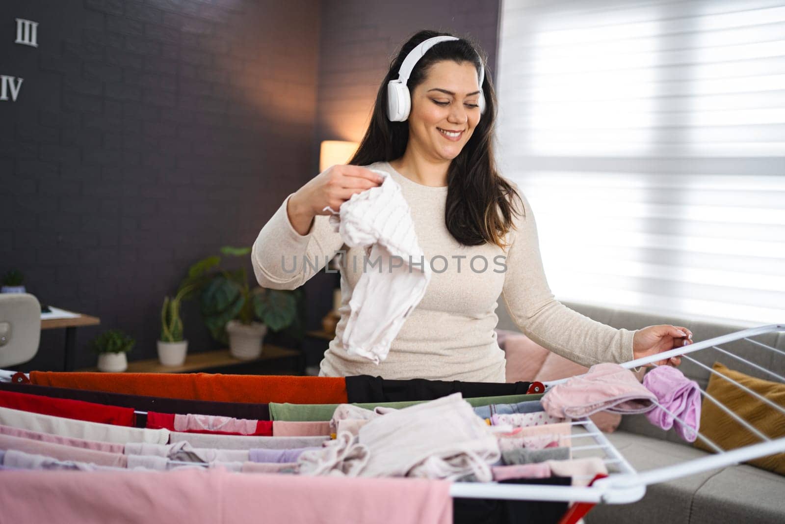 Woman listening to music while hanging the laundry on drying rack at home.