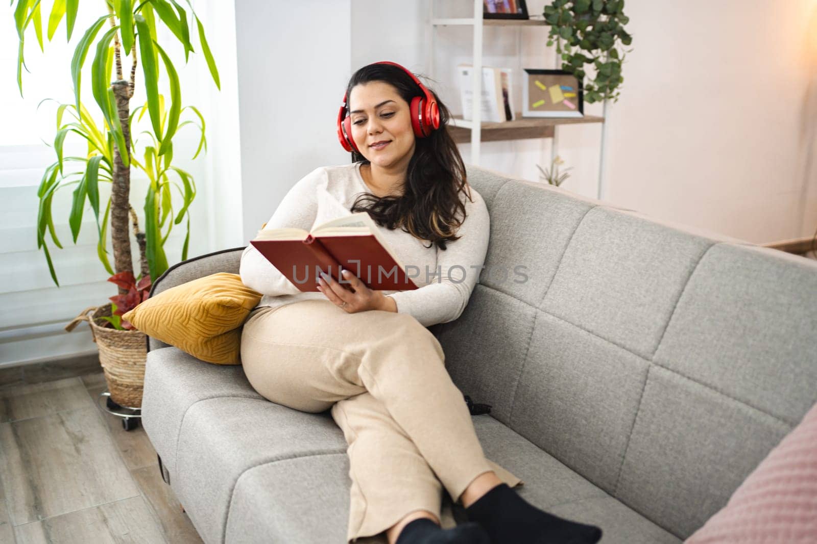 Woman with wireless headphones reading a book on a sofa.
