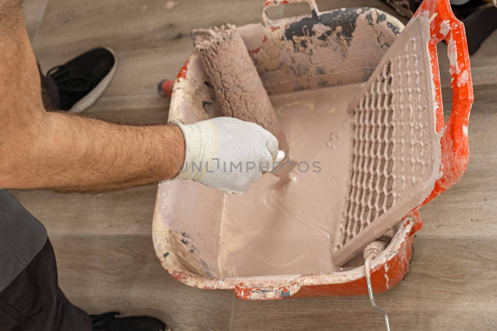 Close up of the container with paint and the paint roller. A man dips a paint brush into the container of paint.