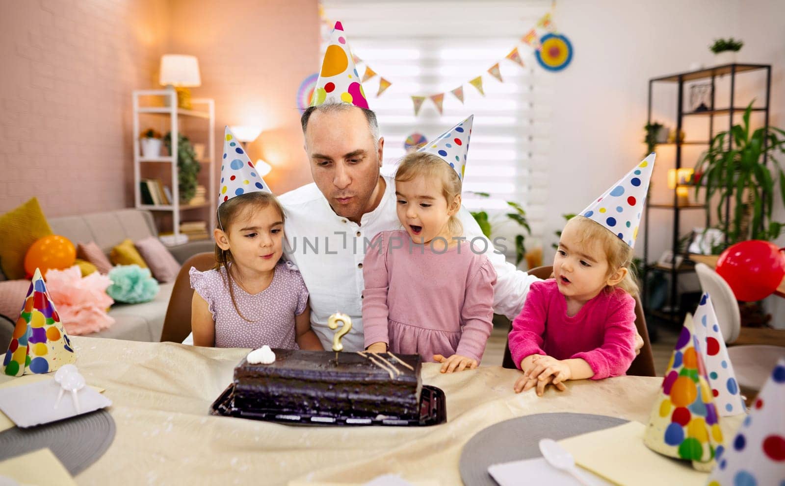 A father shares a joyful moment with his daughters on a birthday.