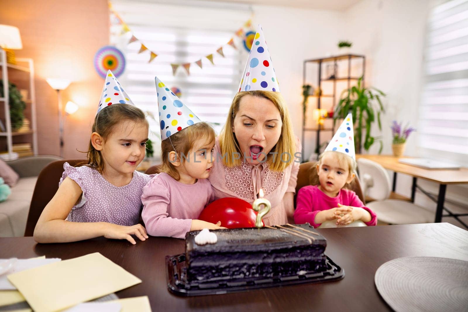 A woman and three young girls celebrate a birthday with cake and balloons.