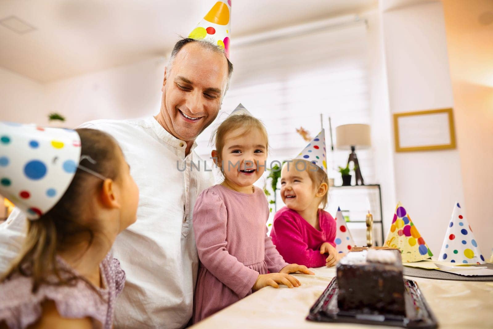 Children in party hats share laughter and cake with a smiling adult.