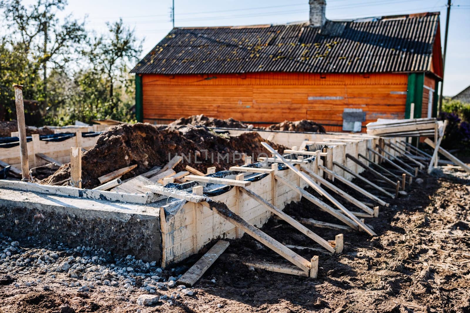 Construction workers building strip foundation for new house near old wooden house