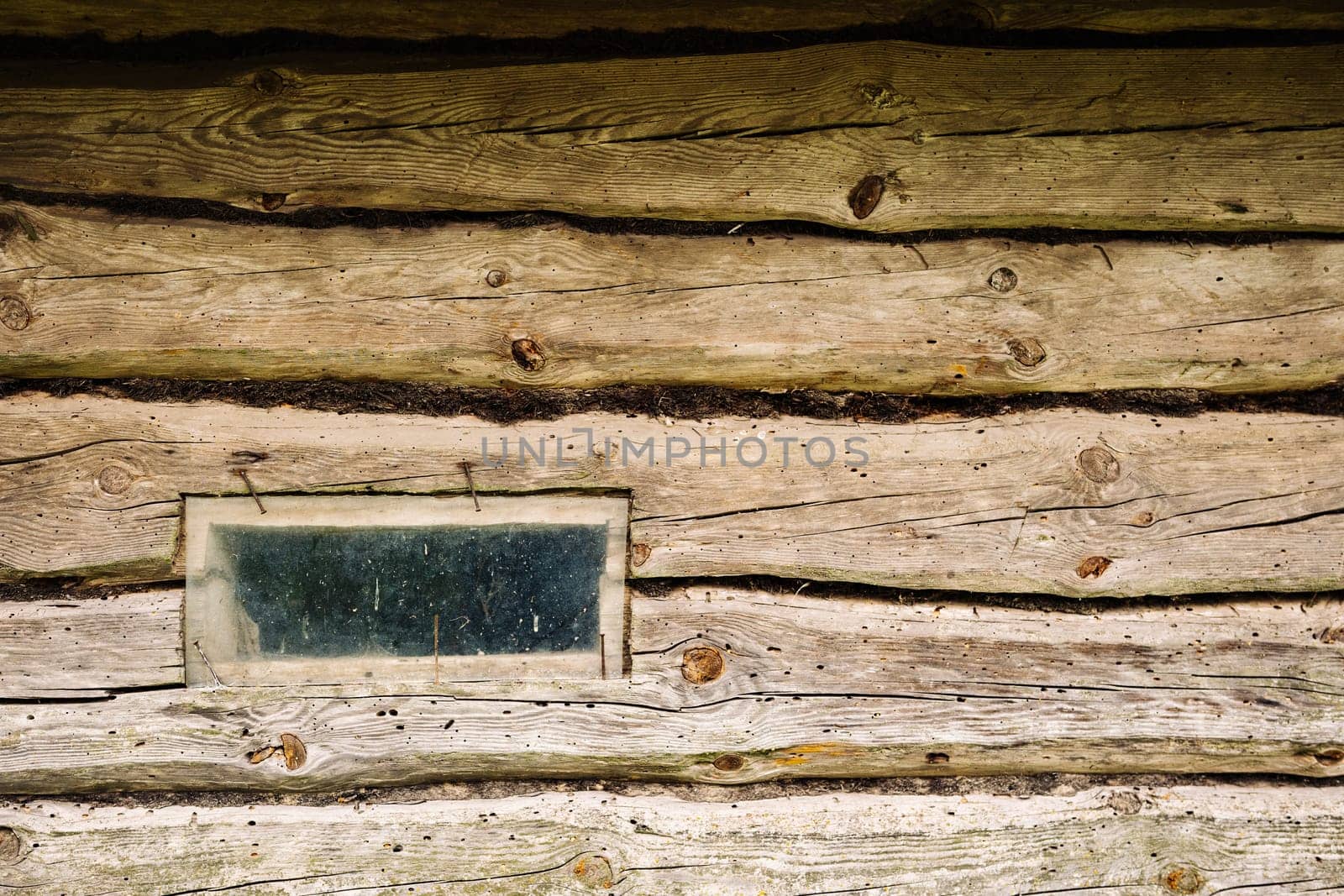 Old weathered wooden wall with small dirty window of abandoned house in countryside